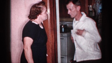 1955: man trying to dance with a woman in a house, with a woman cooking