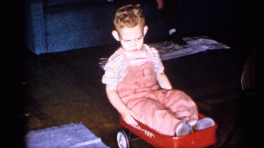 1955: a small boy sitting in a play trolley that is being pulled by his mother