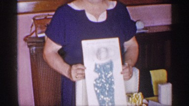 1955: a woman wearing blue happily holding up a piece of artwork NEW YORK