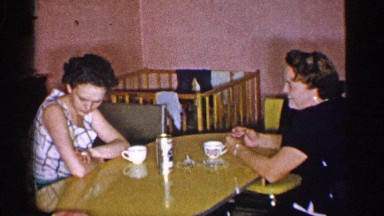 1955: two ladies are talking and eating something at their dining table