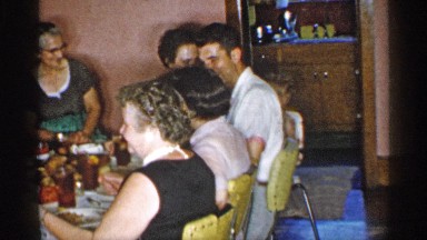 1955: happy family, mainly adults, passing food around the table and eating