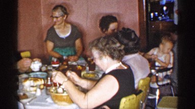 1955: people having dinner to gather and grandmother take care of grandson