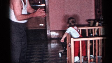 1955: a man in a tank top claps and entertains a baby in a crib NEW YORK