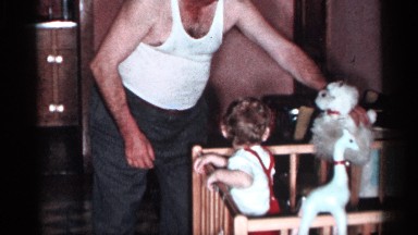 1955: an old man holds a white plush and make play a baby in a crib who watch