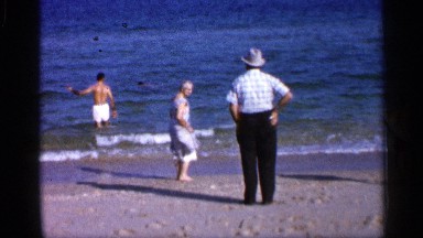 1958: women playing at sea shore watched by her husband and two more bathing