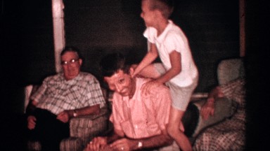 1958: a little boy stands up in the seat to wrap his legs around a young man