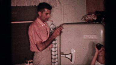 1958: Man Opens Refrigerator Door as Boy Tilts Head Back Holding Bottle