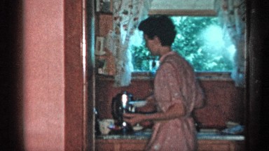 1955: woman walking in a kitchen while dad plays with the baby in another room.