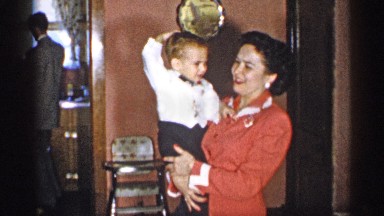 1955: woman holding a baby while other walk in the kitchen. NEW YORK