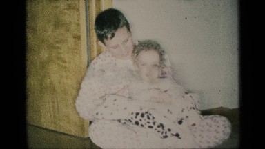 1959: boy holds younger child and stuffed animal on top of his folded legs