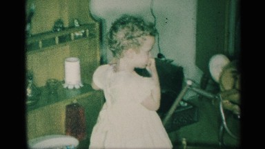 1959: A Small Child Eats and Plays with Toys Near a House