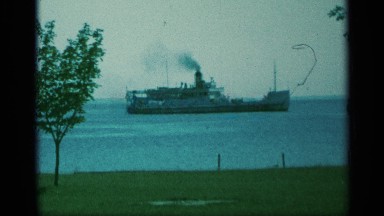 1959: ship emits billowing dark smoke while floating near grassy coastline