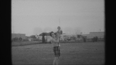 1959: mom holding baby outside and strolling off as dad lifts baby up