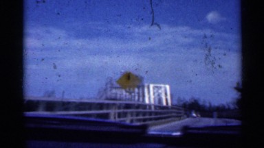 1959: a car approaching a huge and lengthy steel bridge built on the highway