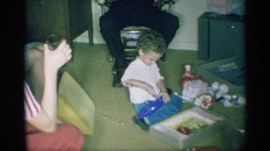 1959: a family watches a young child opening gifts and playing with toys