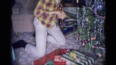 1959: an older man and a teen aged boy are opening and passing out gifts