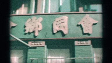 1959: panned city street view, with buildings, people, signs, on hazy day.