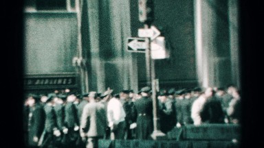 1959: soldiers crowded together marching across a road, while people watch.