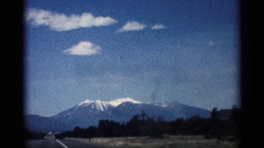 1959: view of a mountain topped with snow during a car ride down a long road.