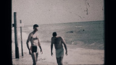 1959: two adult men at the beach with sizable waves and a boy runs past them