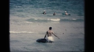 1959: a man in walking in the water while holding a black tube in his hand