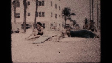 1959: the women and man take the sun both in beach near to sand back side tree