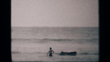 1959: two children at the playing with a floater in the ocean at the the edge.