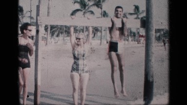 1959: man shows off woman by doing pull ups by the beach . CALIFORNIA