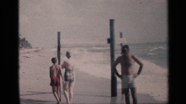 1959: a family stands around poles embedded in a beach as the surf flows around