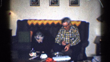 1959: older couple is seated on settee with crocheted zigzag cover on back