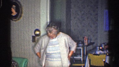 1959: a old lady standing and touch her cloth the men sit and watched that lady