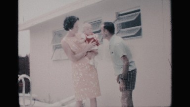 1959: happy family of three with their dog laughing beside the swimming pool