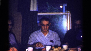 1959: an old man looks like having some in his eyes eating dinner with people
