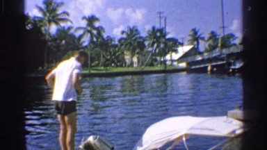 1959: tropical foliage surrounds a body of water and boats and people in summer