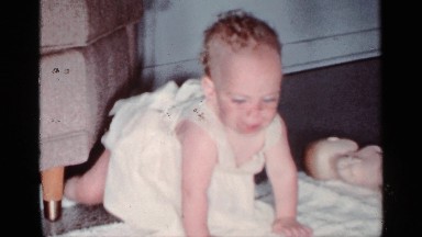 1959: Baby Girl in White Dress and Shoes Leans on Arms and Tries to Crawl