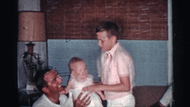 1959: man holding a baby while a young boy approaches and tickles the infant