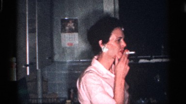 1959: a pink color shirt dressed modern young women smoking a cigarette inside
