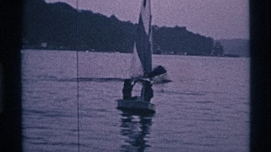1969: pleasure boats, including a sailboat at full sail, across a calm body
