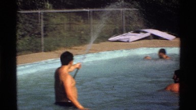 1978: a man sprays water from a hose while other people play in the pool
