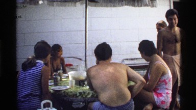 1978: family eats and relaxes at round table with open umbrella in patio