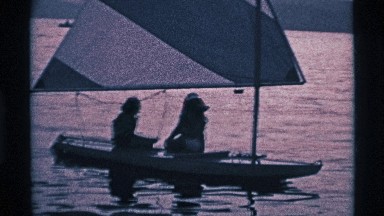 1969: Two Figures Seated on Narrow Sailboat Floating Under Striped Sail Ohio