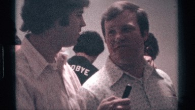 1976: two peoples were talking to each other one holding a pen in a party