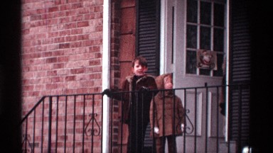 1970: a young boy and his smaller sister stand on their porch on a winter's day