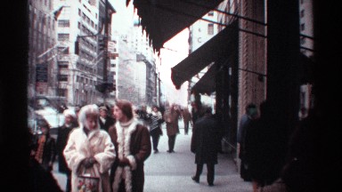 1970: people, some smiling, conversing, wearing warm clothes, walking on a busy