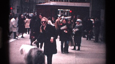 1971: lady walks her dog in the city, the dog is curious about the stroller