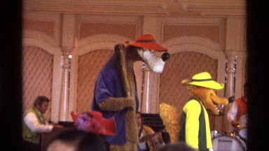 1974: exterior, with stage, instruments, people in costume, heads of watchers.