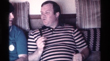 1976: two men seated on a couch talk while one holds a microphone