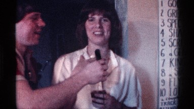 1976: boy holds microphone in front of a black haired woman, passes it around