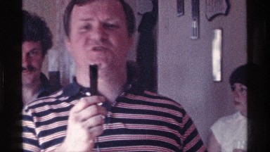 1976: man speaking into a black microphone with people standing