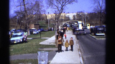 1969: a girl holds her mom, and her brothers hand as she walks down the street